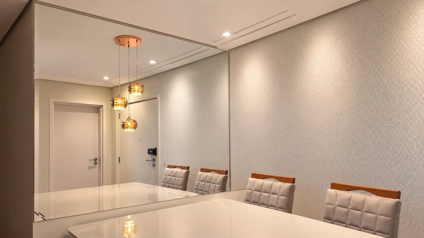 Espelho grande na parede da sala de jantar, refletindo o lustre e a porta